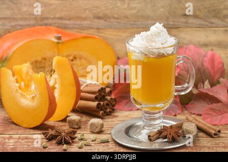 Frullato di latte con spezie di zucca con panna montata e cannella in tazza di vetro su fondo in legno. Tradizionale colazione autunnale calda o fredda Foto Stock