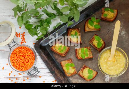 Delizioso pane tostato con hummus (paté, pasta, salsa) di lenticchie e carote con germogli di pisello. Colazione salutare. Messa a fuoco selettiva Foto Stock