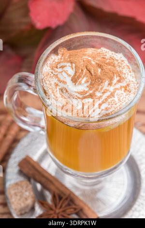 Frullato di latte con spezie di zucca con panna montata e cannella in tazza di vetro su fondo in legno. Tradizionale colazione autunnale calda o fredda Foto Stock
