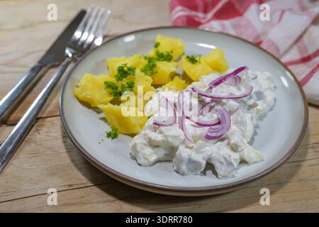 Insalata di aringhe in panna acida con cipolle rosse, servita con patate da giacca e guarnita con prezzemolo su un piatto e un rustico tavolo in legno, tradizionale Foto Stock