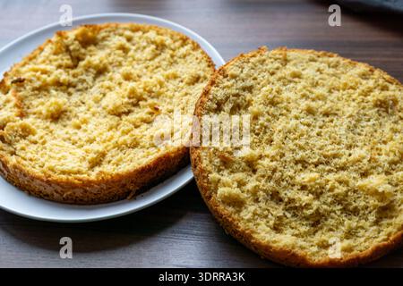 Due strati rotondi di pan di Spagna vengono tagliati orizzontalmente e posizionati su un piatto. Le morbide briciole ariose e la crosta dorata sono chiaramente visibili in primo piano. Foto Stock