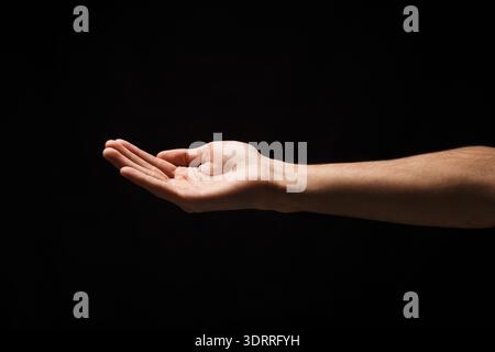 Mano aperta in attesa di un oggetto in un'impostazione buio con messa a fuoco sul gesto Foto Stock