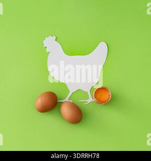 Composizione creativa di uova fresche naturali con uova e tuorlo incrinati su sfondo verde chiaro. Spazio per la copia delle note della sagoma di pollo. Foto Stock
