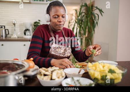 Donna che indossa le cuffie per preparare verdure sane in cucina Foto Stock