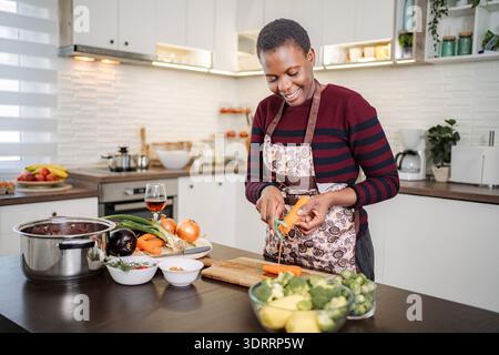 Donna pelare la carota in una cucina moderna e luminosa preparando cibo sano Foto Stock
