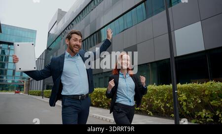 Felice uomo d'affari caucasico donna in città lavoro a piedi buoni risultati celebrano successo uomo d'affari di successo donna d'affari spensierata insieme Foto Stock