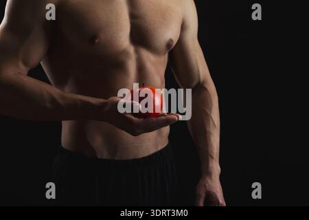L'uomo tiene in mano la mela rossa su sfondo scuro con Focus on Body e Fruit Foto Stock
