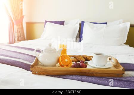 La colazione viene servita su un vassoio in una camera d'hotel con luce soffusa del mattino che arriva attraverso la finestra Foto Stock