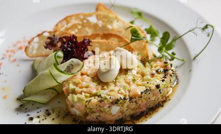 Metti in mostra l'autentica specificità regionale con questa vivace tartare di salmone, caratterizzata da texture locali, verdure fresche e patatine artigianali per un look fedele Foto Stock