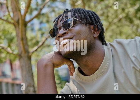 Un bel giovane cammina attraverso un parco animato, sorridendo e crogiolandosi alla luce calda del sole. Foto Stock
