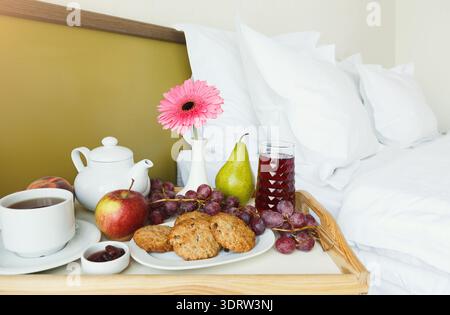 Colazione collage con tè, biscotti, frutta e fiori su vassoio in una camera d'hotel Foto Stock