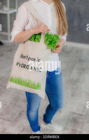 Donna che tiene in mano un sacchetto della spesa in cotone riutilizzabile con lattuga verde fresca visibile. Uno stile di vita ecologico con alimenti biologici. Foto Stock