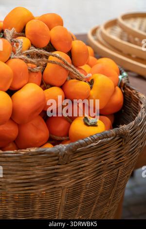 I cachi d'arancia maturi disposti in un cesto di vimini, legati in fasci di spago per un'esposizione autunnale in un mercato rustico Foto Stock