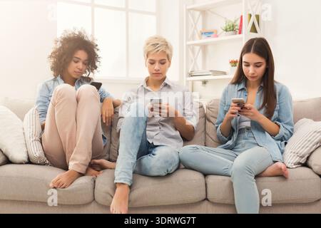 Gruppi di amici che utilizzano smartphone seduti insieme in un'accogliente area soggiorno Foto Stock