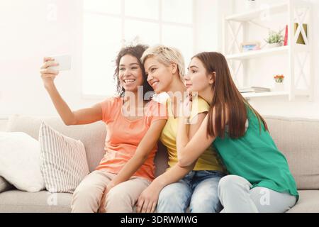 Gruppo di amici che scattano selfie in un luminoso salotto durante un pomeriggio informale Foto Stock