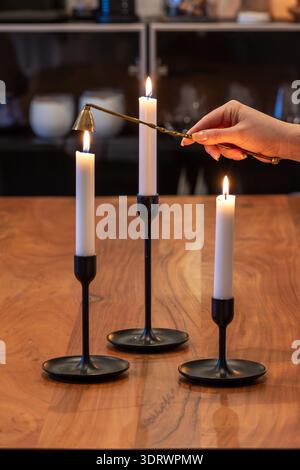 Primo piano di tre candeline accese. Una candela viene spalmata con uno snuffer. Le candele sono bianche su un portacandele nero sulla parte superiore di Foto Stock