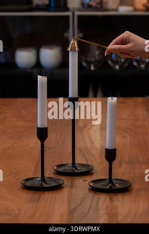 Foto ravvicinata di tre candelabri. Una candela viene spalmata con uno snuffer. Le candele sono bianche su un portacandele nero sopra un woo Foto Stock