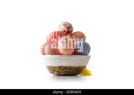 Cestino in tessuto pieno di uova di Pasqua dipinte a mano con motivi floreali, a righe e punteggiati su sfondo bianco con un piccolo flusso di primavera giallo Foto Stock