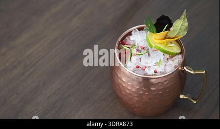 Moscow Mule drink servito in una tazza di rame con ghiaccio e cornici su un tavolo di legno Foto Stock