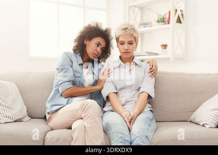 Due amici si siedono insieme su un divano in un accogliente soggiorno, mentre uno offre supporto all'altro Foto Stock