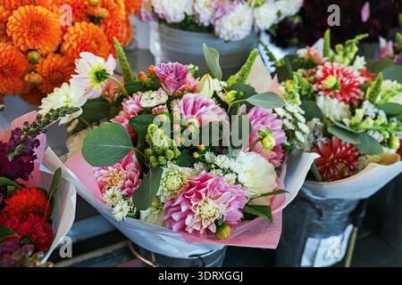 Colorato negozio di fiori con mazzi misti, dahlia rosa, fiori d'arancio e vegetazione avvolta in carta, bassa profondità di campo Foto Stock
