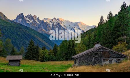 Alta Savoia, Francia - 18 settembre 2025: Tradizionale capanna alpina in pietra e legno con legna da ardere impilata di fronte al massiccio del Monte bianco al tramonto di nea Foto Stock