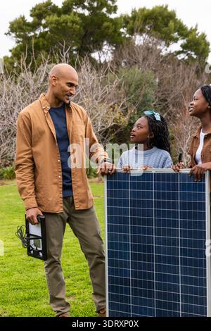 Famiglia afroamericana con cavo inverter di prova pannello solare su prato, bambino in maglione blu Foto Stock