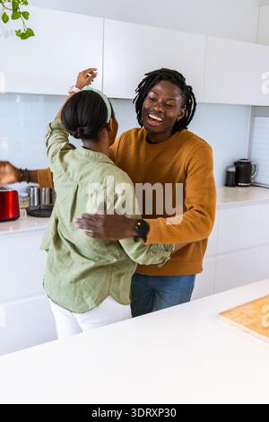 Coppia afroamericana che balla e abbraccia in una luminosa cucina bianca vicino al tagliere Foto Stock