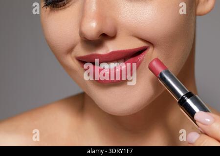 Una donna sorride mentre applica il rossetto alle labbra in un ambiente termale mentre si prende cura della sua routine di cura della pelle. Foto Stock