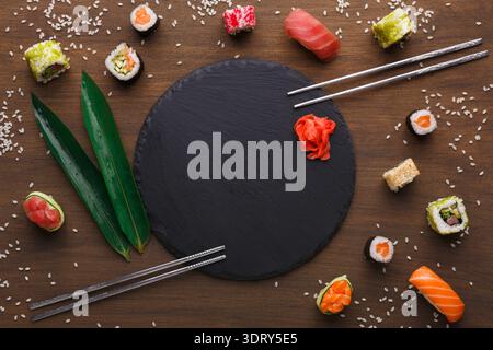 Collezione di sushi disposta su un tavolo di legno con piatto di ardesia e bastoncini neri Foto Stock