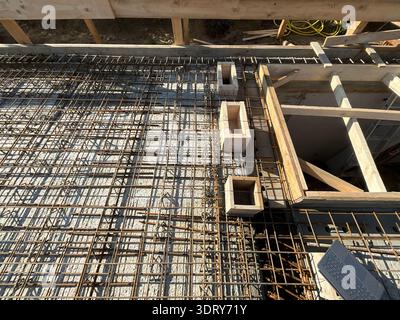 Vista dall'alto della preparazione delle solette in cemento armato in un cantiere residenziale. La rete di armature in acciaio è installata su strati isolanti e legno f Foto Stock