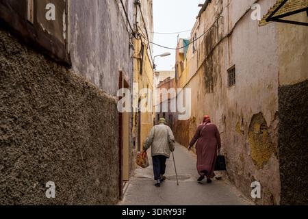 Una suggestiva veduta posteriore di un uomo anziano con un bastone e una donna che camminano lungo uno stretto vicolo nel cuore della Medina di Meknes, un He mondiale dell'UNESCO Foto Stock
