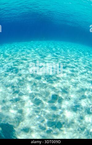 Il sole ondeggia e si riflette sulla sabbia bianca in acque blu poco profonde con cielo blu e raggi del sole Foto Stock