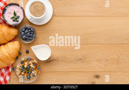 Deliziosa colazione a buffet con croissant, yogurt, mirtilli e caffè su tavolo di legno Foto Stock