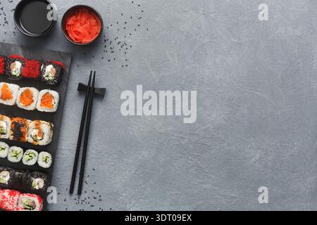 Delizioso sushi preparato su una tavola scura con salse e bastoncini sul lato Foto Stock