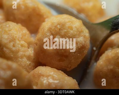 Primo piano di grani rotondi di cereali da colazione con latte, evidenziando la consistenza, il colore e i dettagli dei grani soffiati Foto Stock