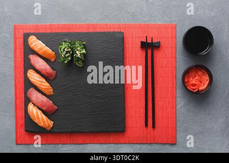 Sushi su un piatto nero con bastoncini e condimenti posti su un tappeto rosso Foto Stock