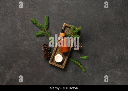Composizione con bottiglia di olio essenziale, rami di abete e coni su sfondo scuro Foto Stock
