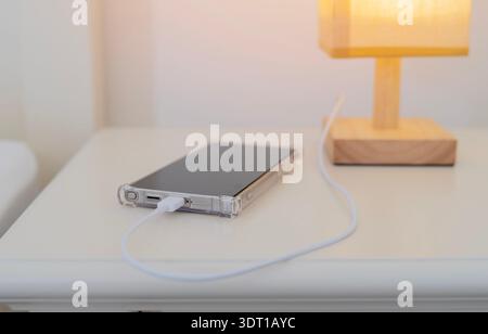 Batteria di ricarica dello smartphone tramite la presa di ricarica usb integrata sul comodino con lampada. Messa a fuoco selettiva. Foto Stock
