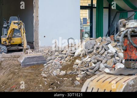 Mucchio di macerie di cemento in primo piano e escavatore in background durante la demolizione e la ricostruzione di proprietà urbane. Foto Stock