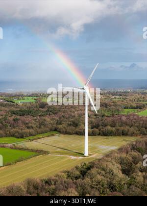 Vista aerea di una sola turbina eolica si erge alta in mezzo a una fitta foresta, coronata da un arcobaleno vibrante, simbolo di energia sostenibile, Tréglamus, Bretagne, Foto Stock
