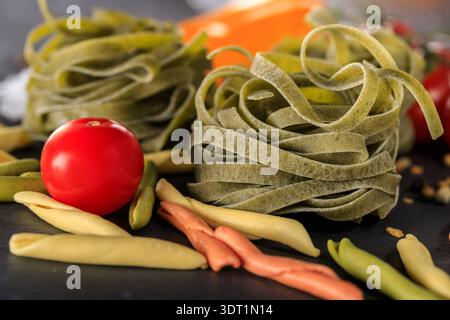 Tagliatelle di pasta cruda agli spinaci e primo piano di pomodoro rosso ciliegia su tavola. Foto Stock