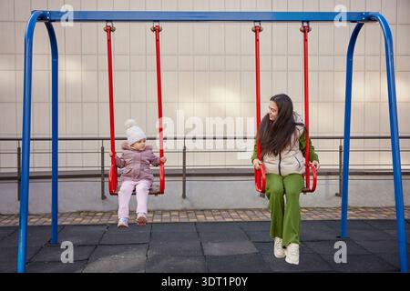 Madre e figlia dondolano, si divertono e si legano al parco giochi Foto Stock