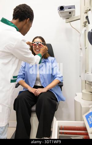 Un ottico esegue un esame oculistico su un paziente utilizzando una cornice di prova in una clinica moderna. Il paziente sorride mentre l'ottico regola le lenti in modo da ottenere un effetto Foto Stock