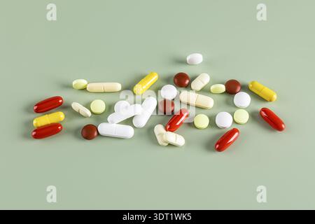 Le pillole colorate assortite e le capsule mediche sono sparse su uno sfondo verde neutro. Questa immagine evidenzia le varie forme farmaceutiche utilizzate Foto Stock