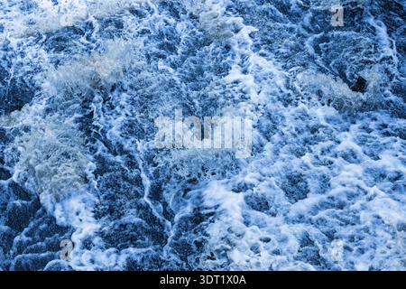 Onde dinamiche e tempestose che creano intricati motivi di schiuma bianca sulla superficie, evocano un senso di energia naturale e un'atmosfera costiera. Sfondo naturale p Foto Stock