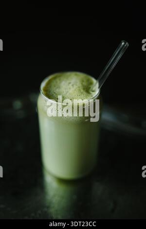 Un rinfrescante latte matcha servito in un bicchiere trasparente con una cannuccia di vetro. La bevanda verde schiumosa viene catturata su uno sfondo scuro, evidenziandola Foto Stock