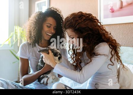 Una coppia gioiosa si siede insieme a casa, tenendo e giocando con amore con il coniglio. La scena cattura un momento di felicità, relax e Foto Stock