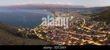Vista notturna aerea di Pogradec, Albania, con luci di strada scintillanti, fitte aree urbane e la tranquilla costa del lago di Ocrida. Foto Stock