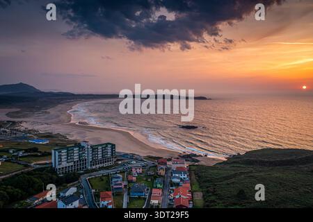 Vista aerea di un villaggio costiero al tramonto con una spiaggia di sabbia curvilinea, dolci onde oceaniche, Valdovino , Spagna Foto Stock